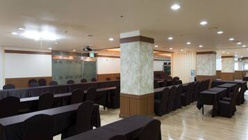 Un salón de conferencias con filas de mesas y sillas, un pilar de mármol y un panel de pared de madera.