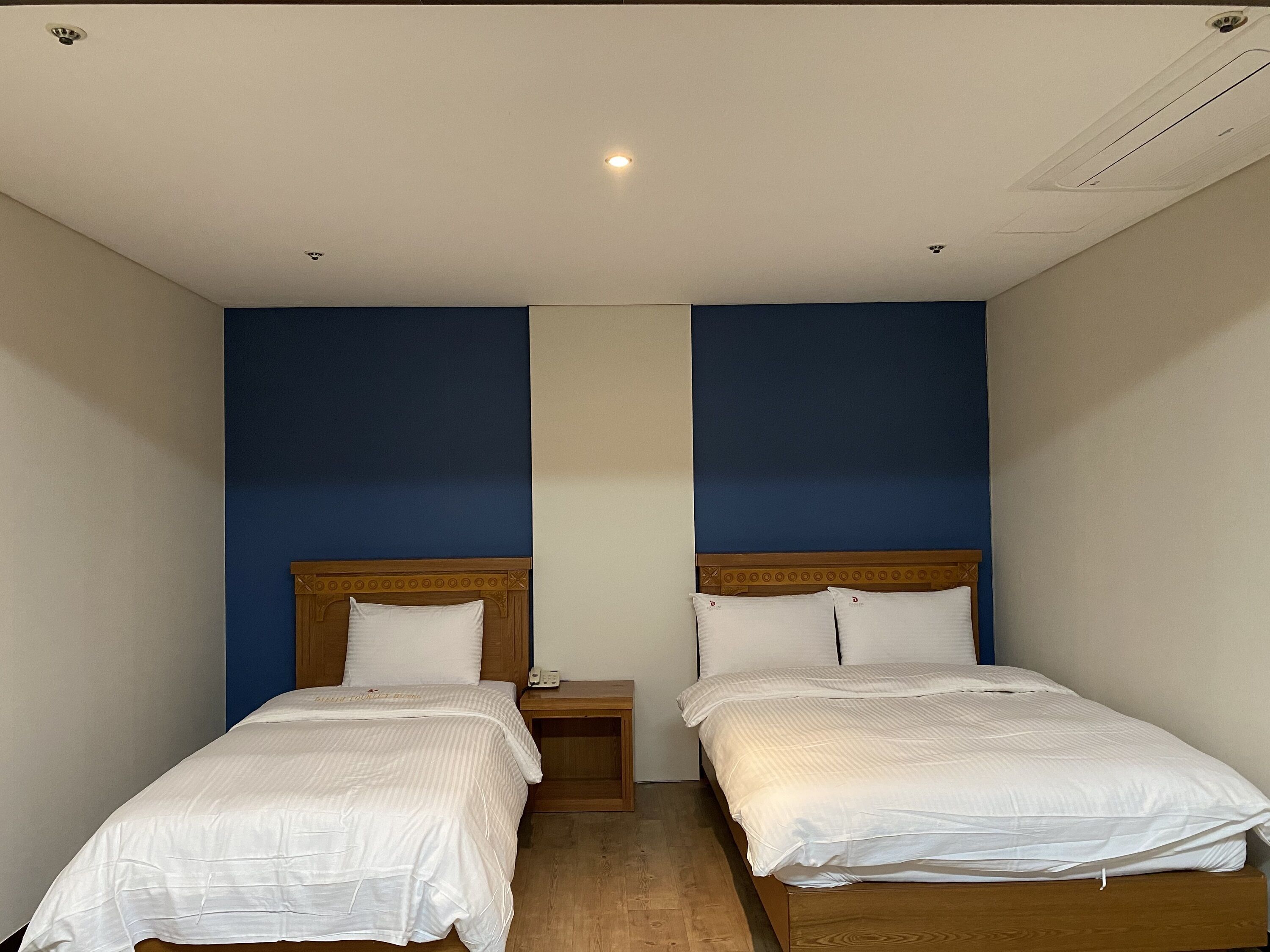 A room with two single beds, wooden headboards, and a small bedside table with a lamp.