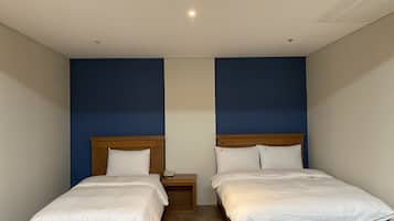A room with two single beds, wooden headboards, and a small bedside table with a lamp.