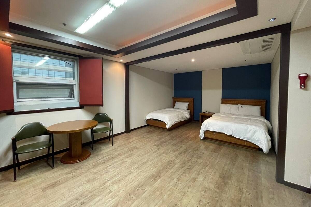 A hotel room with two single beds, a small table with chairs, a window, and a red wall.