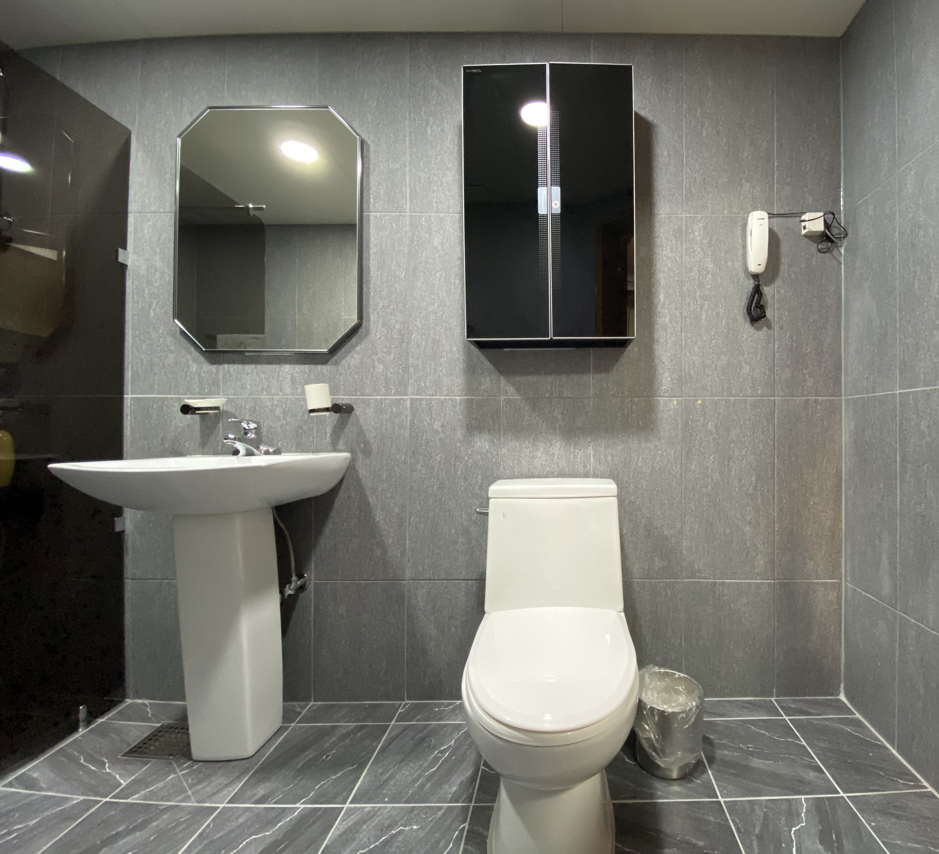 Une salle de bain avec un lavabo blanc, des toilettes, un miroir et un meuble de rangement.