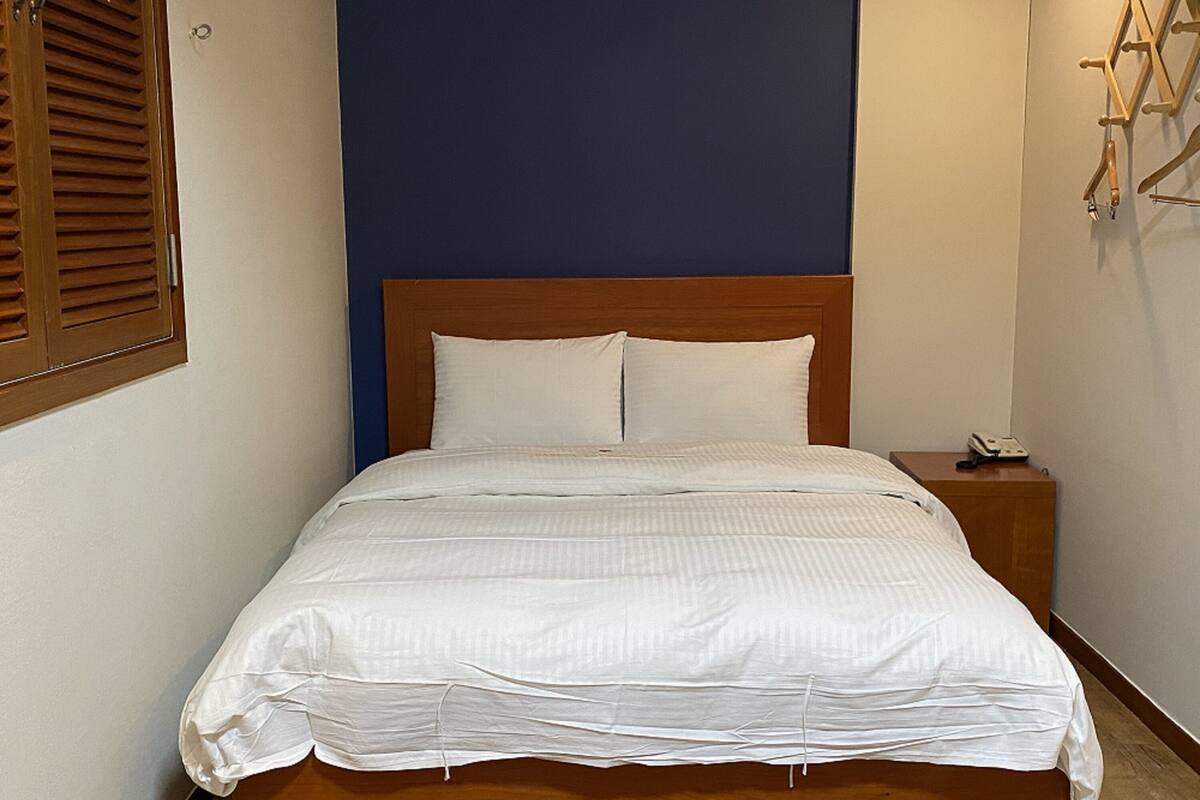 A neatly made bed with a wooden headboard, a bedside table with a lamp, and a window with wooden shutters.