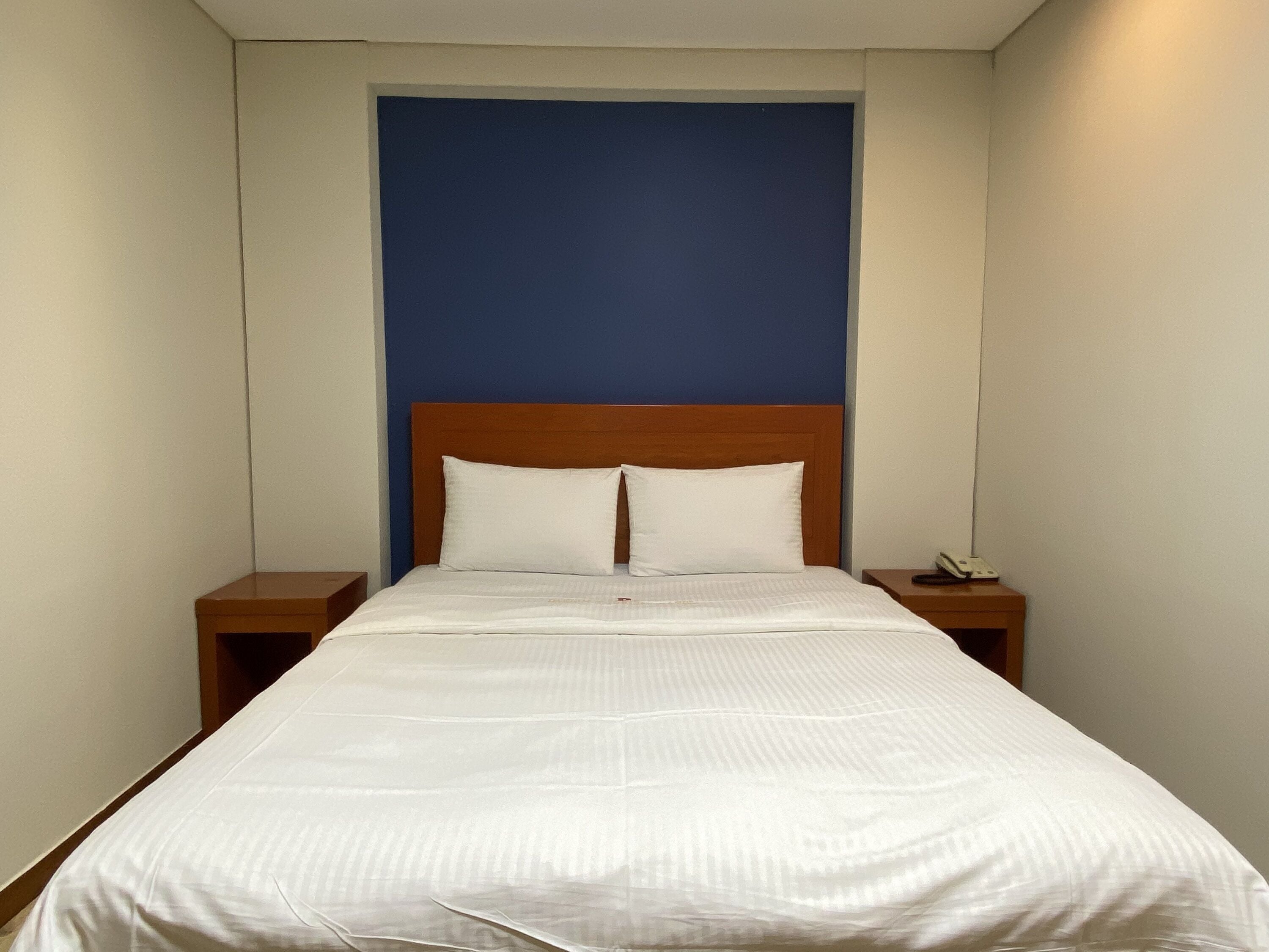 A neatly made bed with white linens, a wooden headboard, and two bedside tables with a phone on one.