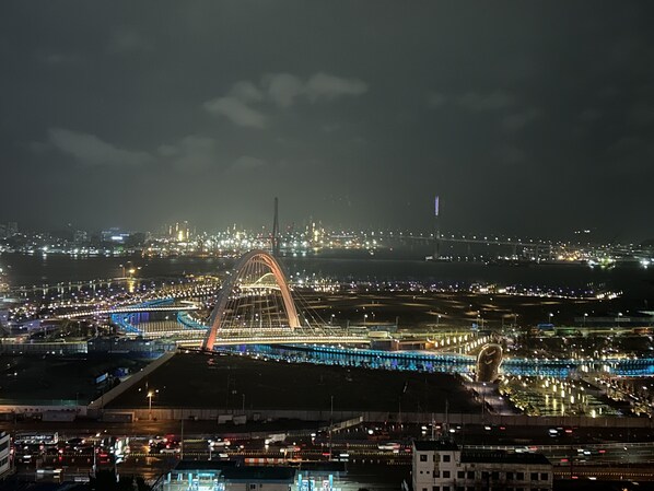 Un paisaje urbano nocturno con un puente iluminado destacado y luces de ciudad lejanas.
