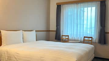 Una habitación de hotel con una cama grande, dos sillas, una ventana con cortinas translúcidas y una lámpara en el techo.
