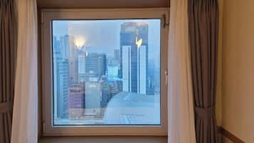 A hotel room with a large window offering a cityscape view, including a hotel and tall buildings.