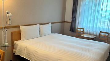 Una habitación de hotel con una cama grande, un escritorio con lámpara, una silla y una mesita.