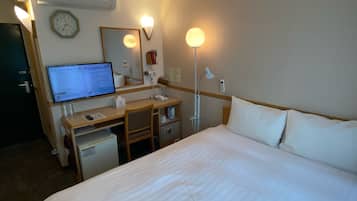 A hotel room with a bed, desk, chair, computer, and a small refrigerator.