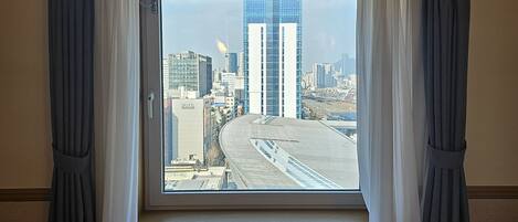 A hotel room with a large window offering a view of a cityscape, including tall buildings and a road.