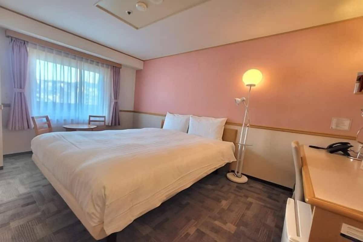 A hotel room with a large bed, a desk, a chair, and a lamp.