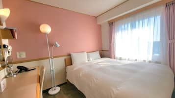 A hotel room with a large bed, a desk with a lamp, and a window with curtains.