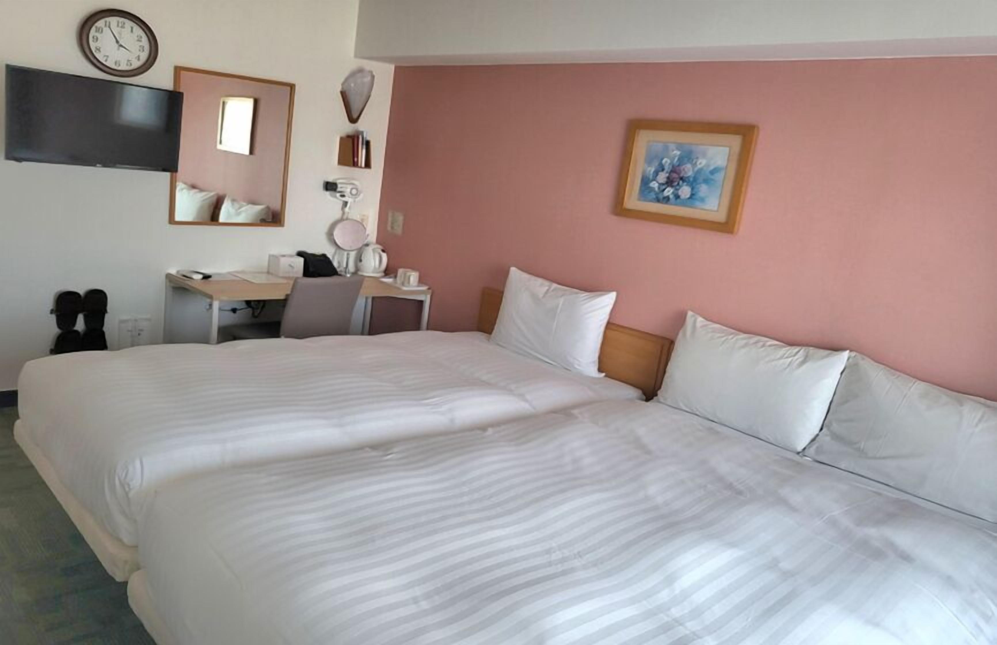 Una habitación de hotel con una cama grande, un escritorio, una silla, un televisor y un reloj en la pared.