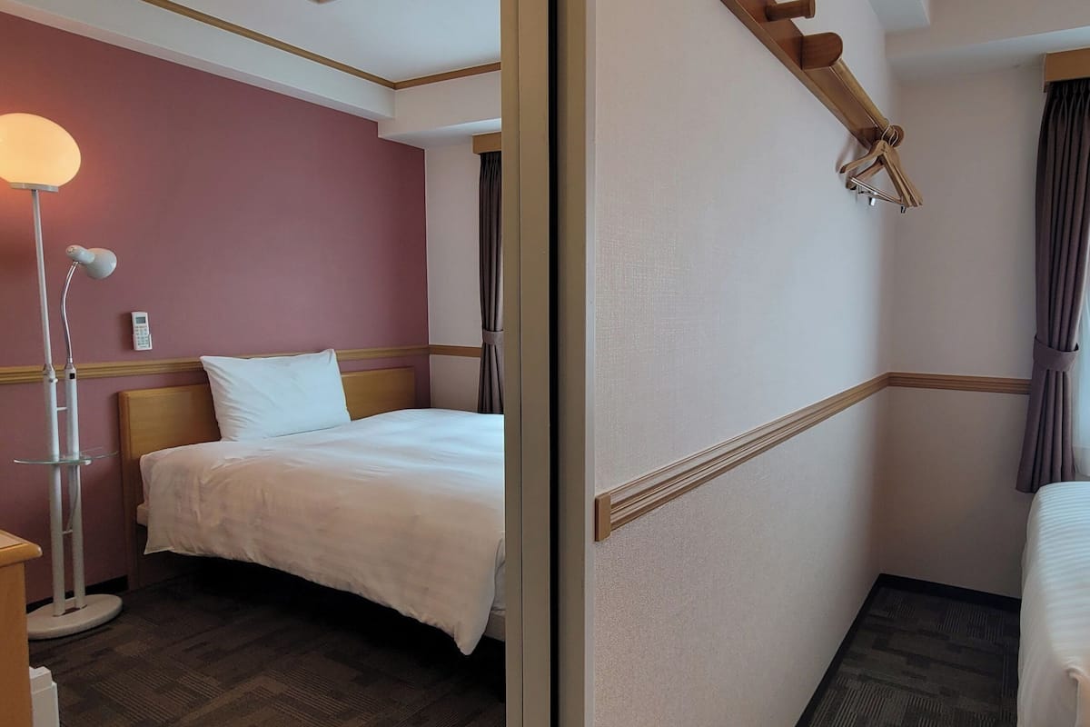 A hotel room with two beds, a bedside table, a lamp, and a window with curtains.