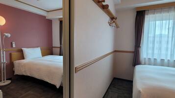 A hotel room with two beds, a bedside table, a lamp, and a window with curtains.