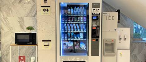 Máquina expendedora con varias bebidas y un microondas sobre una encimera de baldosas de mármol.