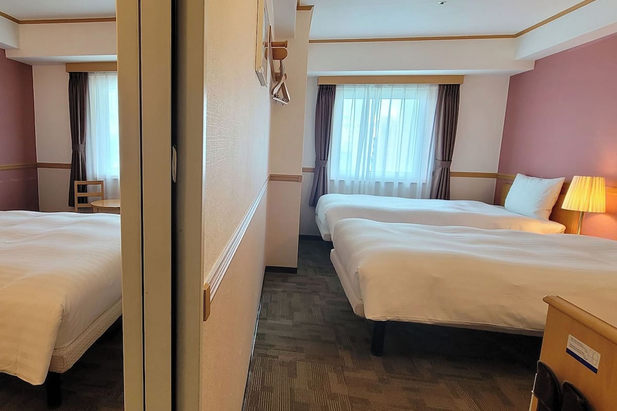 A hotel room with two beds, a small table, and a chair.