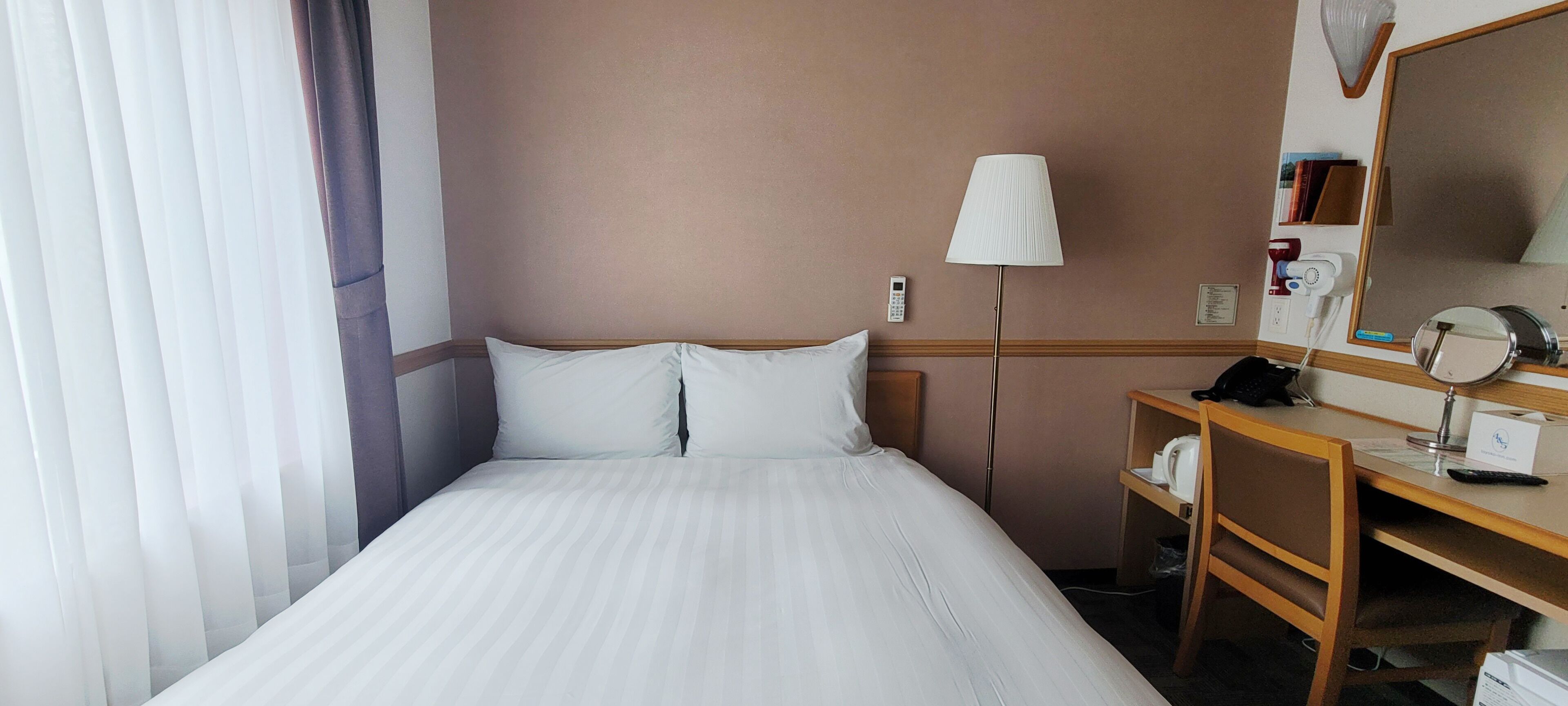 A hotel room with a bed, a desk with a lamp, a mirror, and a phone.