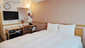 Habitación de hotel con cama, escritorio, teléfono, espejo, reloj y televisión.
