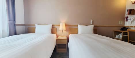 A hotel room with two single beds, a bedside table with a lamp, a phone, and a shelf with a kettle and cups.