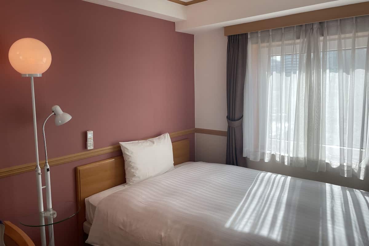 A hotel room with a bed, a bedside lamp, a telephone, and a window with curtains.