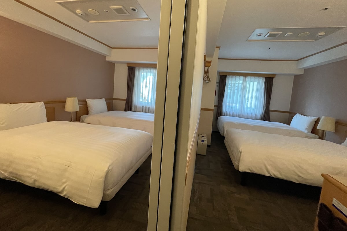 A hotel room with two beds, a mirror, and a ceiling with light fixtures.