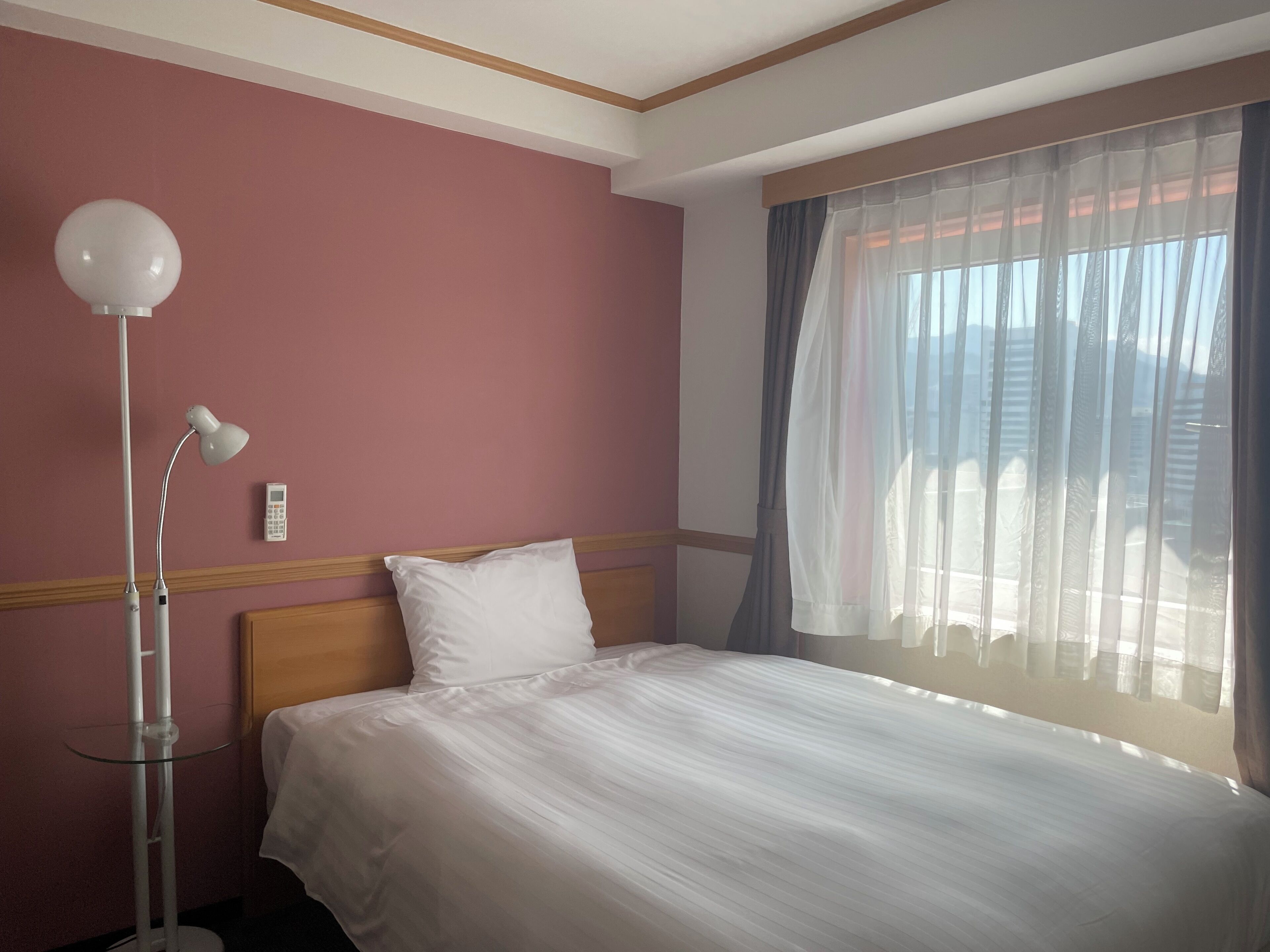 A hotel room with a bed, a bedside table, a lamp, and a window with curtains.