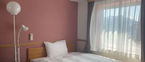 Una habitación de hotel con una cama, una mesita de noche, una lámpara y una ventana con cortinas.