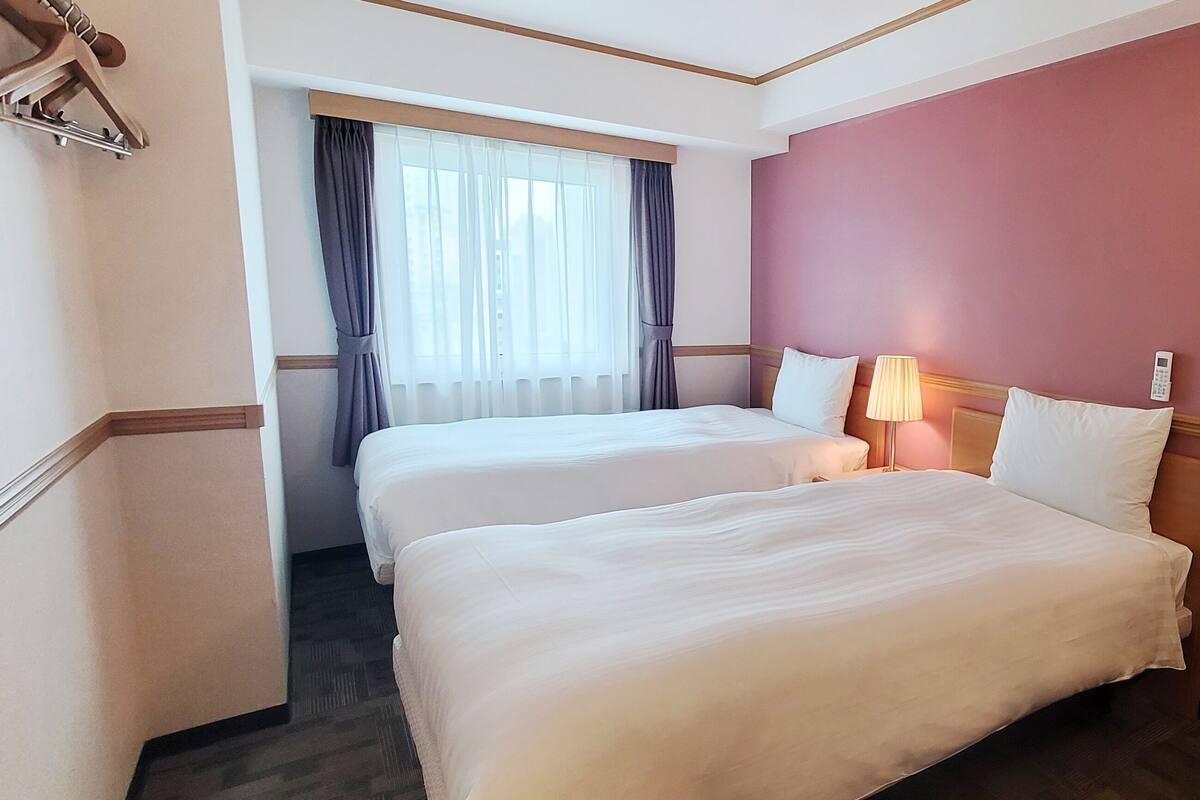 A hotel room with two beds, a desk, a chair, a lamp, and a telephone.
