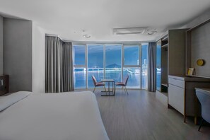 Une chambre d’hôtel avec un grand lit, un bureau, une chaise et une vue sur la ville et l’eau.