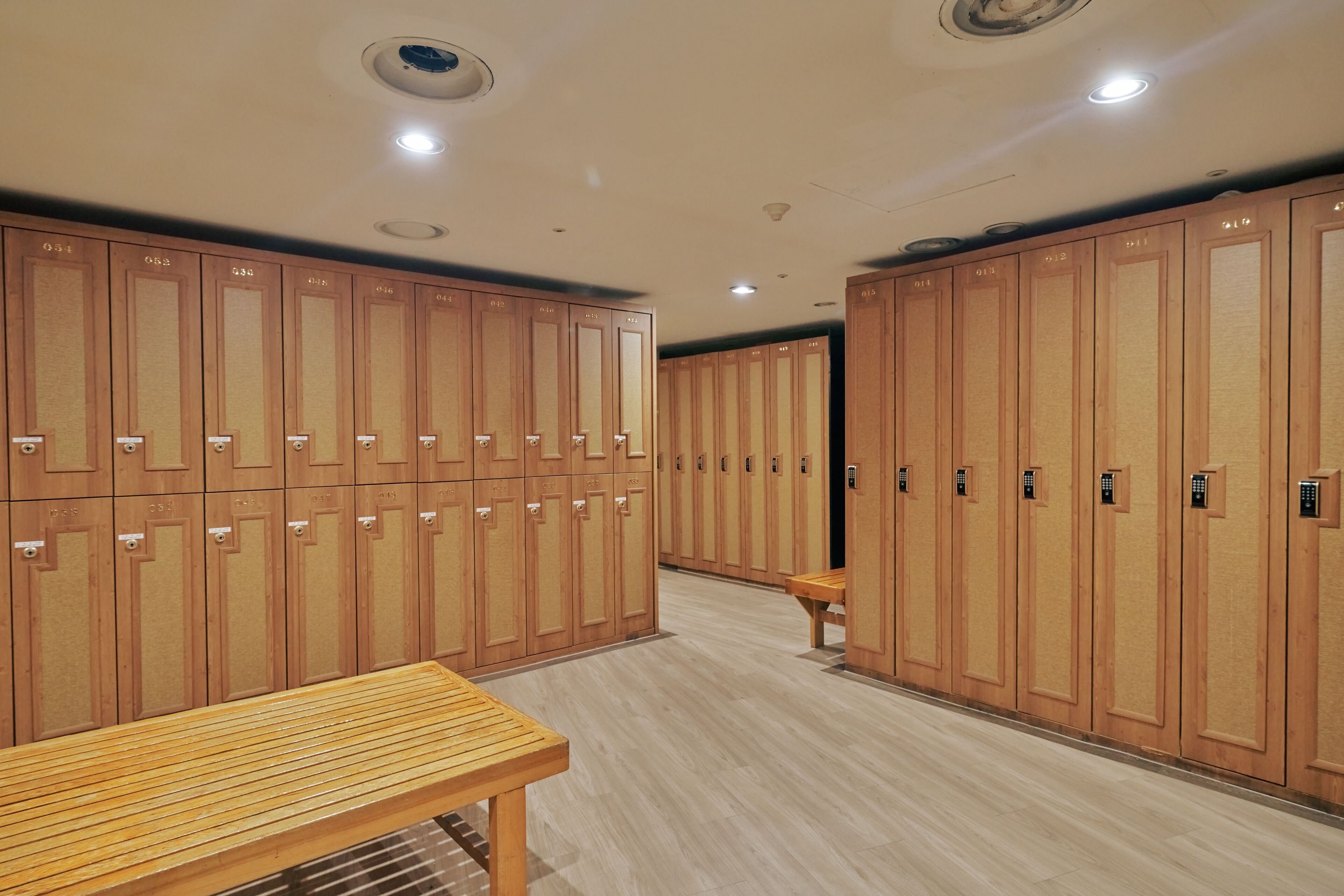 Una hilera de taquillas de madera con puertas numeradas, un banco de madera y un piso de baldosas.
