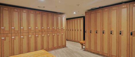 Una hilera de taquillas de madera con puertas numeradas, un banco de madera y un piso de baldosas.