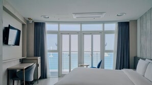 A hotel room with a large bed, a desk with a chair, a television, and a view of the sea through large windows. - Hotel Aqua Palace (Busan)