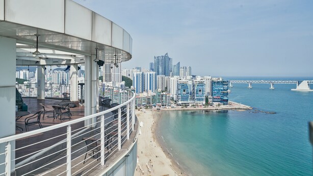 A rooftop terrace with a city skyline and a beach in the background. - Hotel Aqua Palace (Busan)