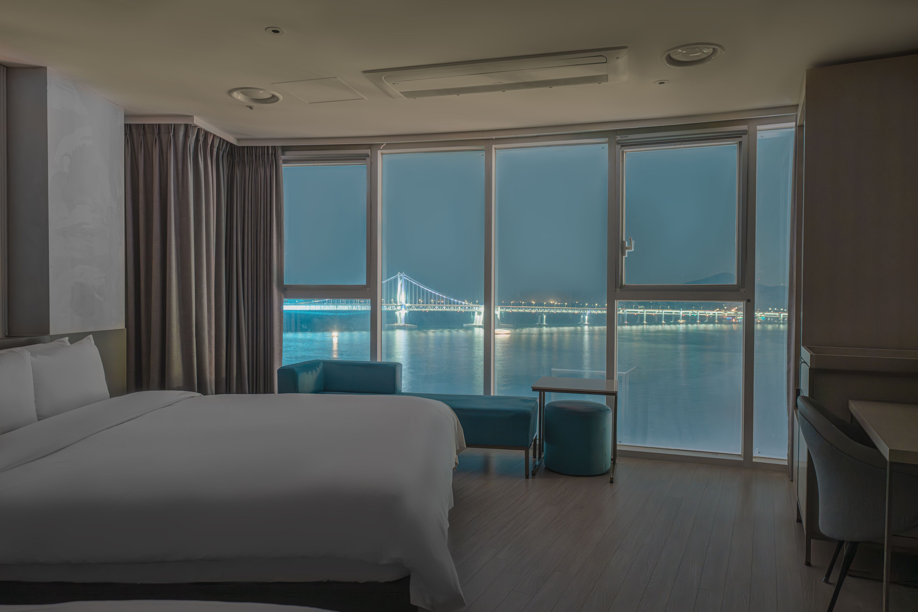 A hotel room with a large bed, a desk, a chair, and a view of a bridge over water.
