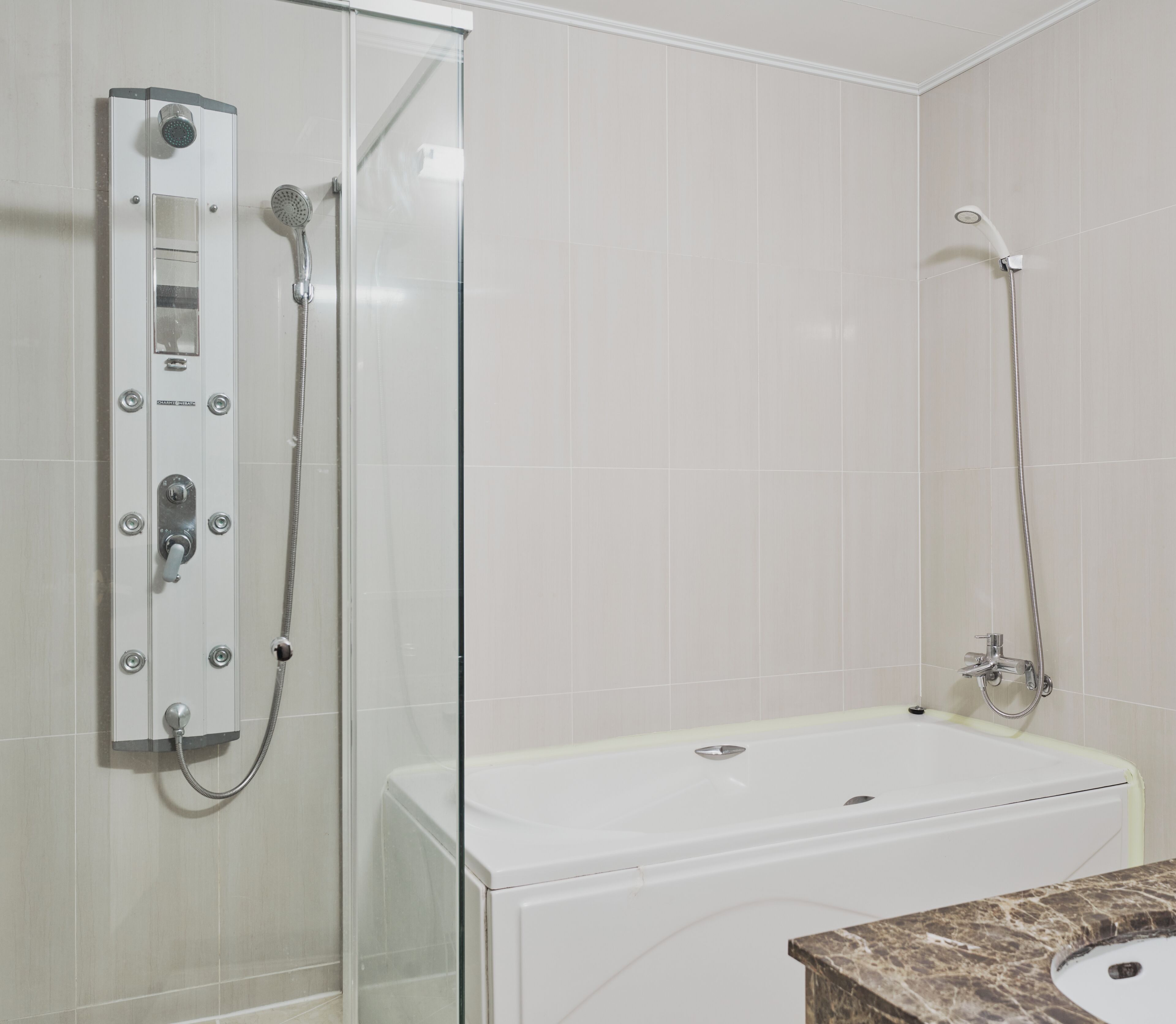 A bathroom with a glass-enclosed shower, a white bathtub, and a marble countertop with a sink.