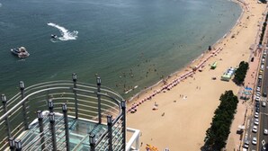 A beach with a curved promenade, a pool, and a view of the ocean. - Hotel Aqua Palace (Busan)