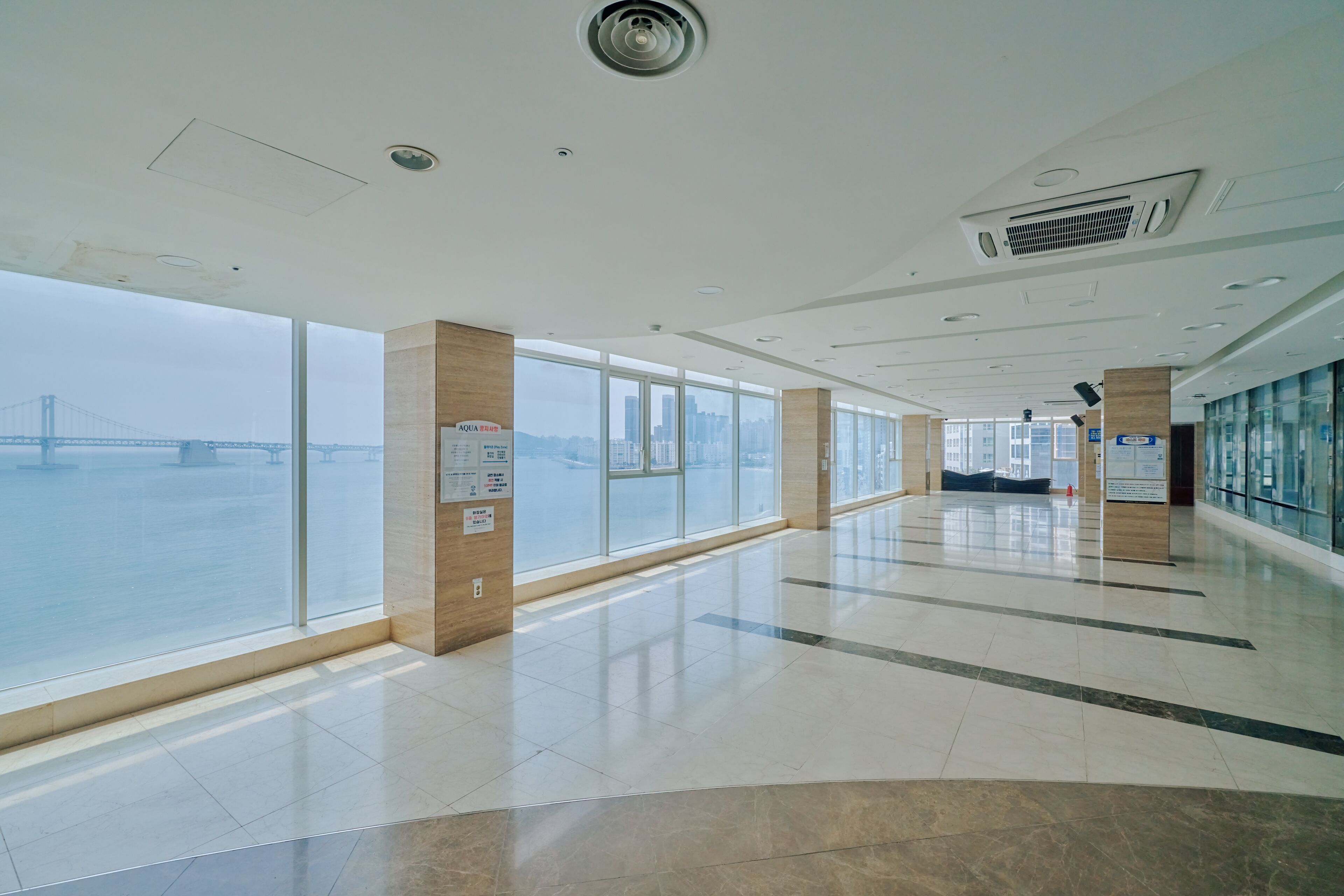 Corredor amplo com grandes janelas que oferecem vista para uma ponte e o horizonte da cidade.