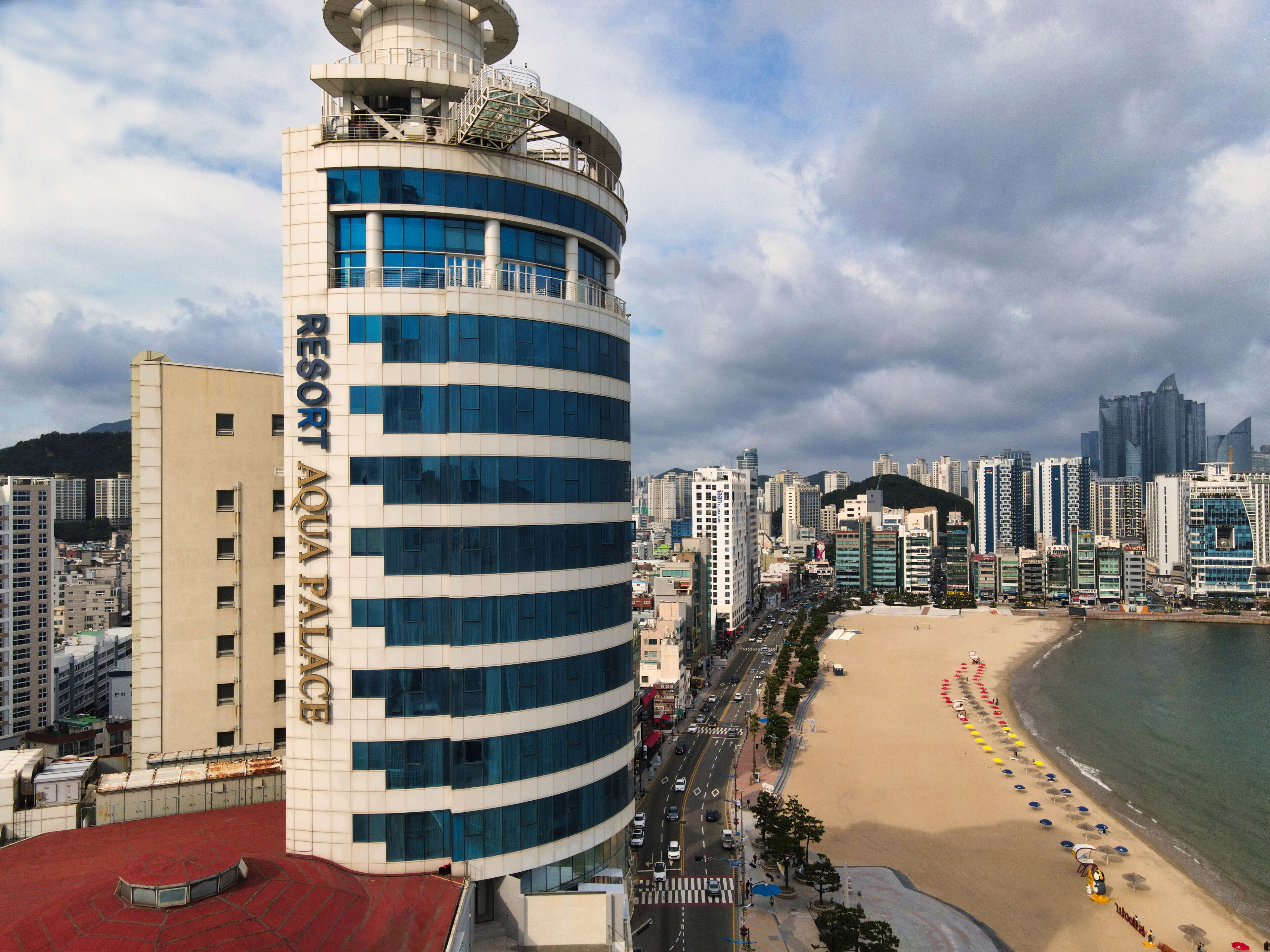 Um hotel moderno com fachada curva, terraço no telhado e vista para a praia.