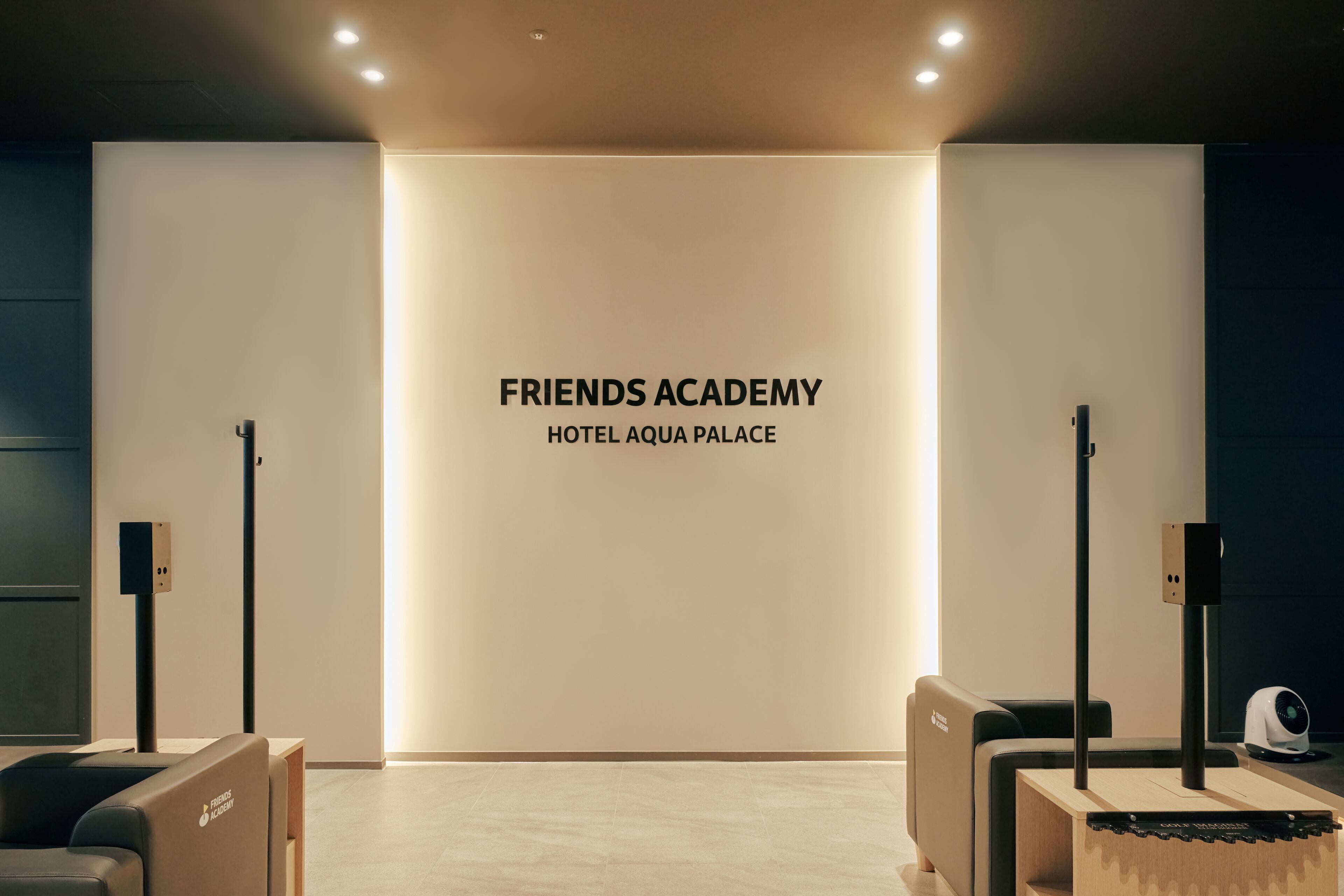 A modern lobby with a minimalist design, featuring a large illuminated sign for the Friends Academy Hotel Aqua Palace.