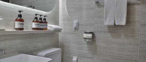 Une salle de bain moderne avec un lavabo, des toilettes et une douche, le tout de couleur blanche. On peut voir des flacons de produits de toilette sur le comptoir, et des serviettes sont suspendues à un porte-serviettes.