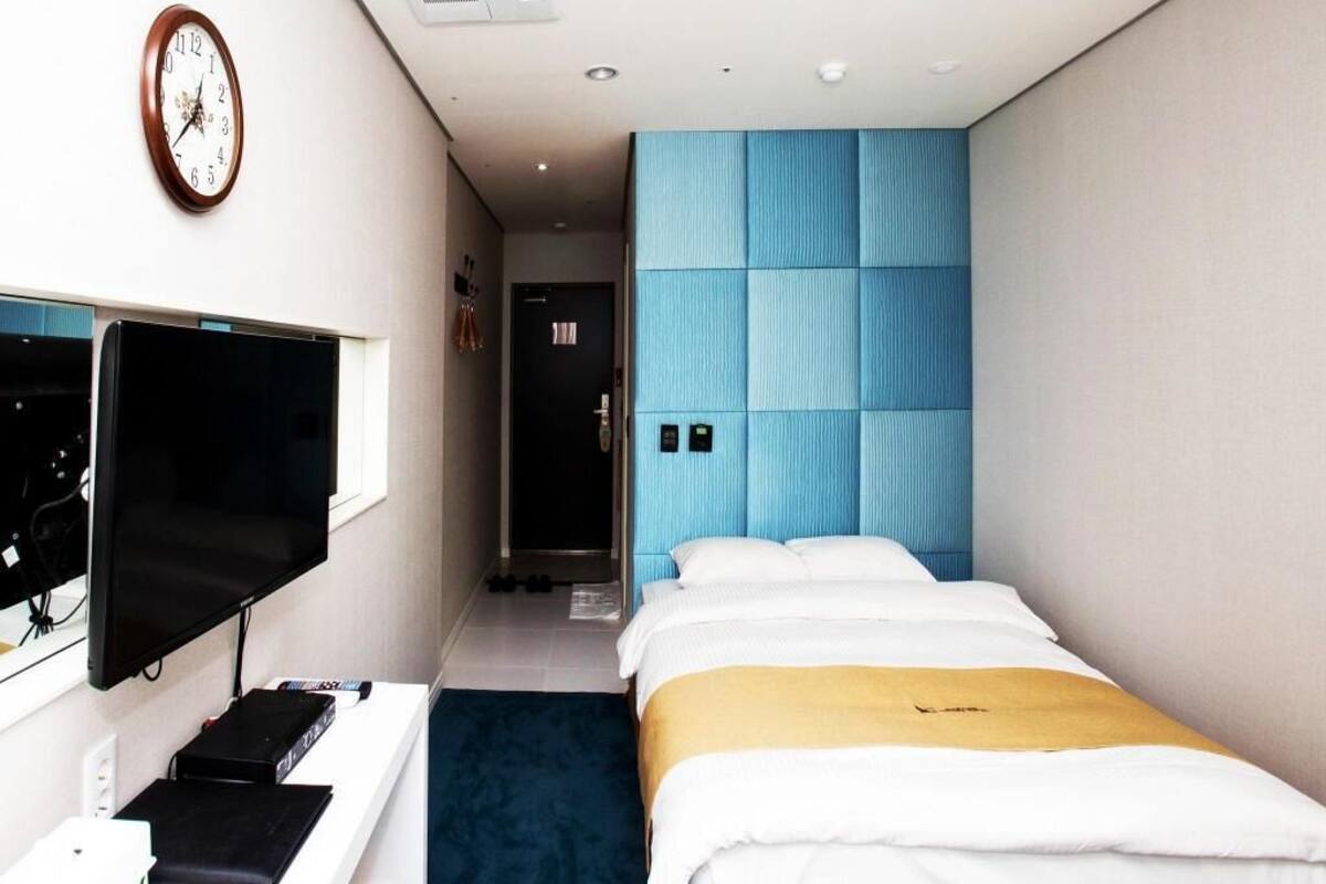 Una habitación de hotel con una cama, televisor, escritorio con computadora y un reloj en la pared.
