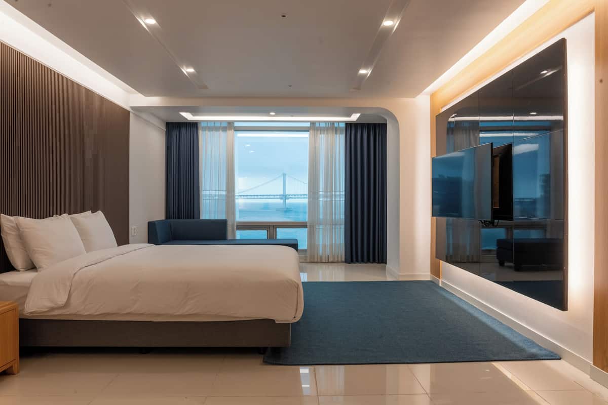 A modern hotel room with a large bed, a TV, and a view of a bridge.
