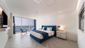Ein modernes Hotelzimmer mit einem großen Bett, einem Schreibtisch, einem Sessel und Meerblick.