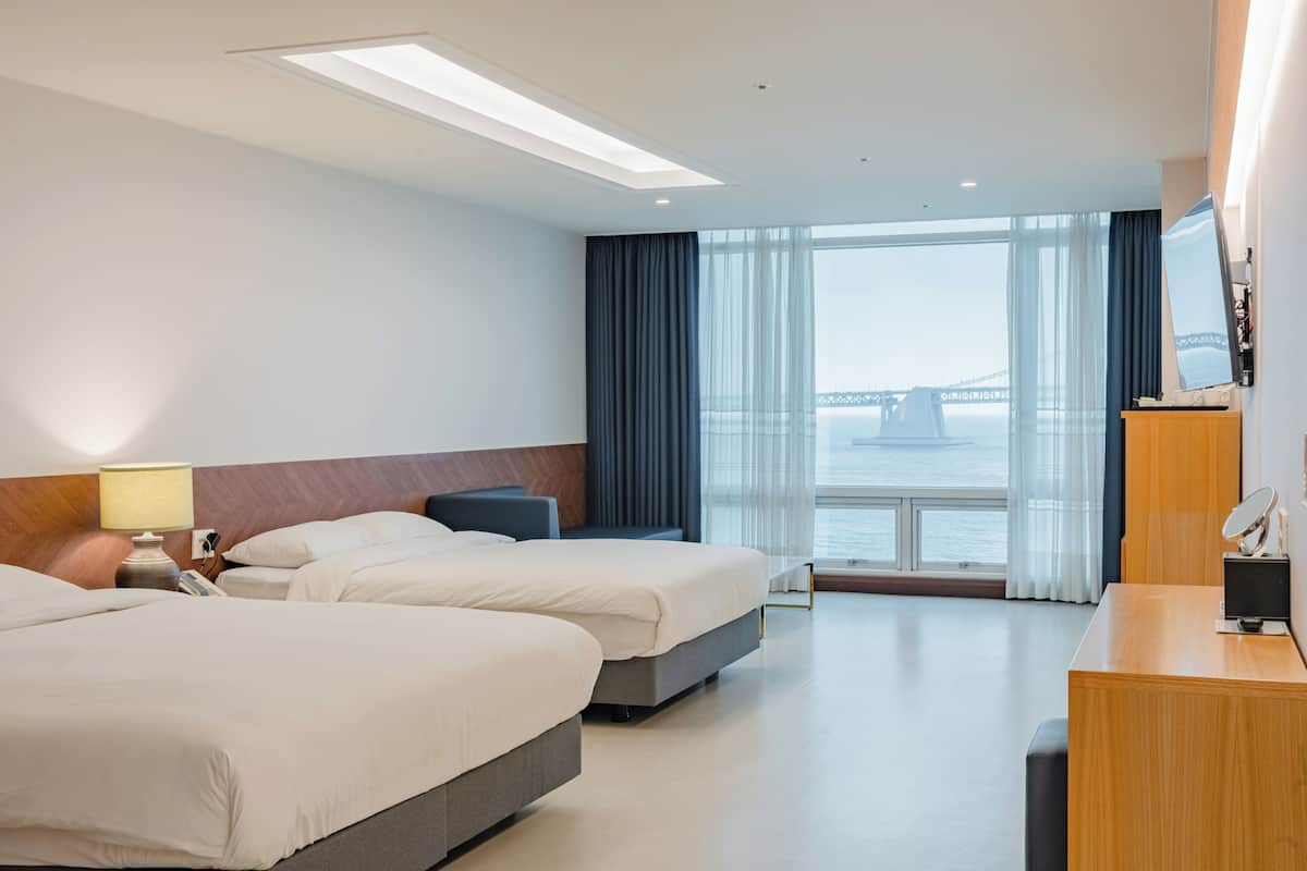 A hotel room with two beds, a desk, a TV, and a view of a bridge.