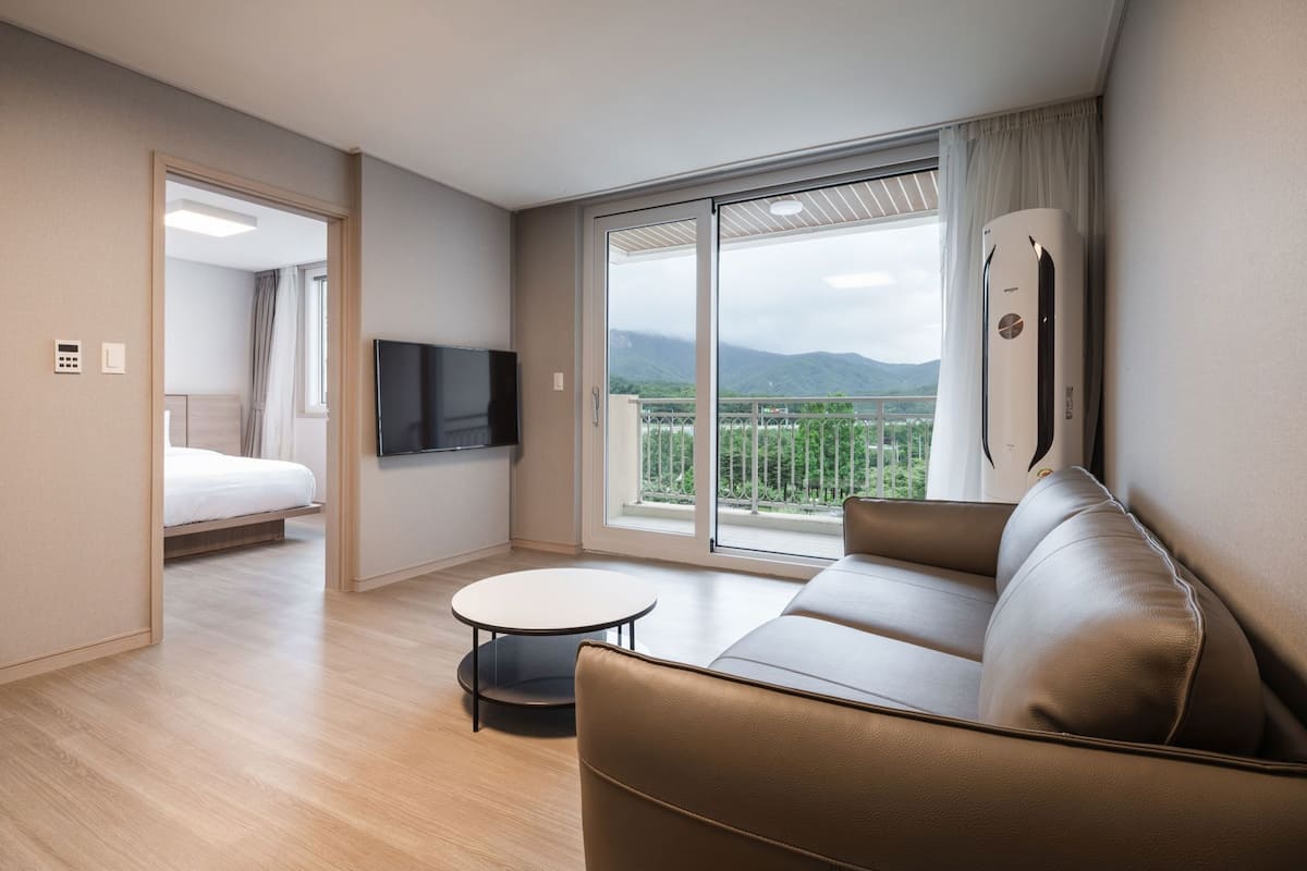 Habitación de hotel moderna con cama, sofá, televisor, balcón con vistas a la montaña y puerta corrediza.