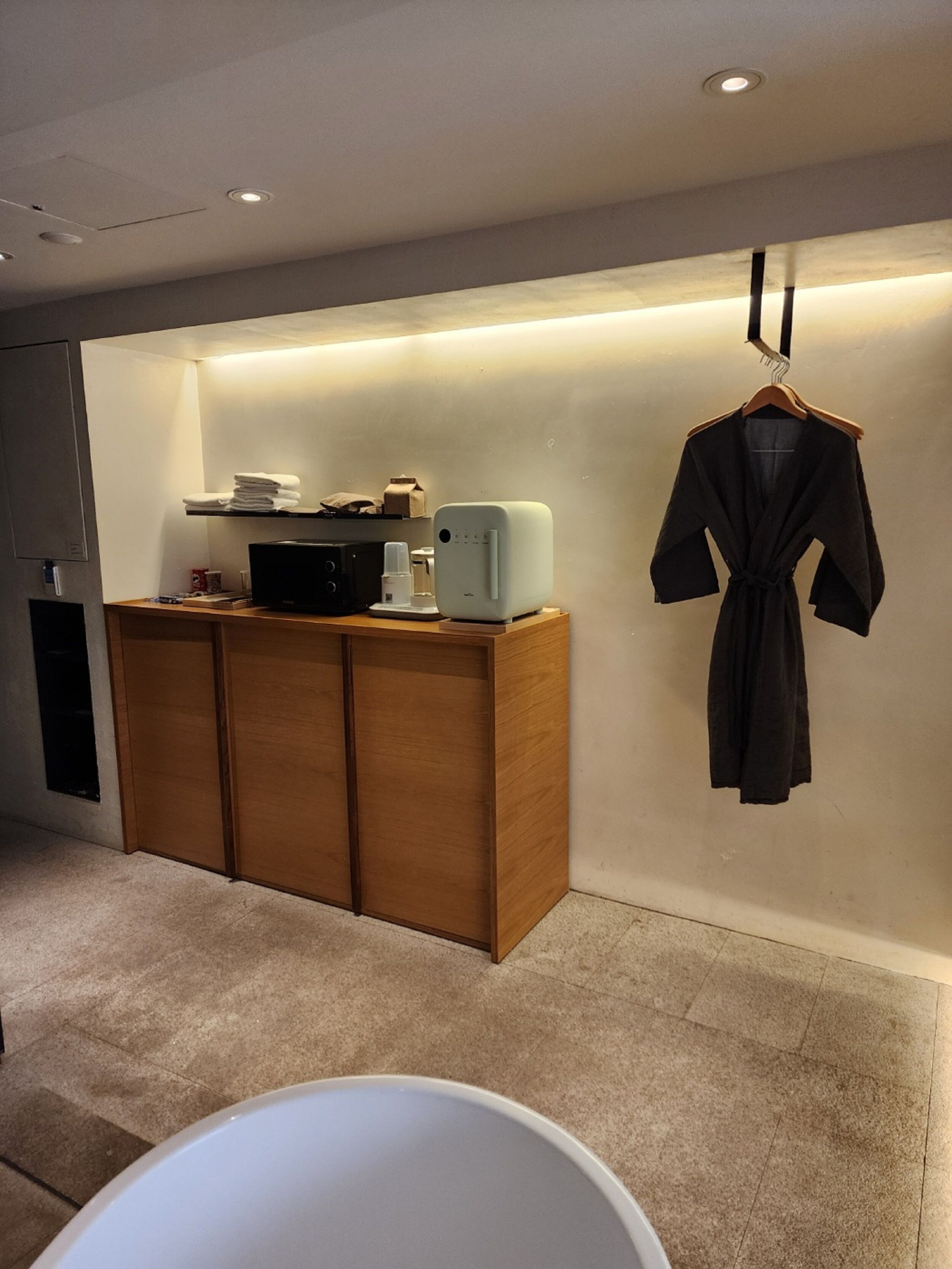 Un baño moderno con tocador de madera, una bañera blanca y una bata colgada en la pared.