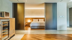 A modern hotel room with a wooden floor, a bed with white linens, a nightstand with a lamp, and a minibar. - Phoenix Hotel Pyeongchang (Pyeongchang)
