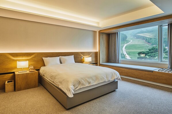 A hotel room with a large bed, bedside tables with lamps, a window with a view of a green landscape.