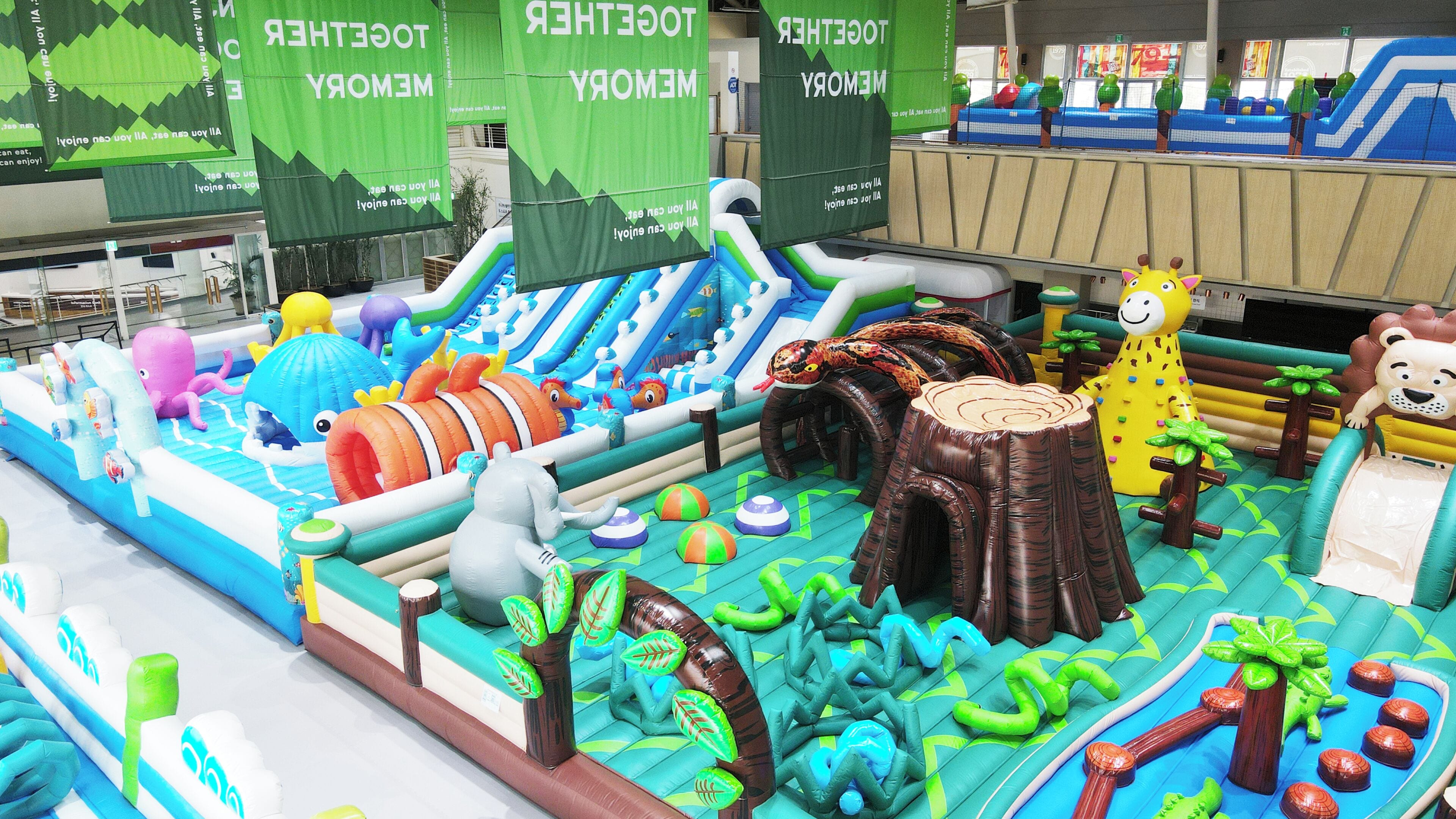 Un espace de jeux intérieur comprenant des toboggans gonflables, des structures de jeux sur le thème de la jungle et un grand arbre gonflable.
