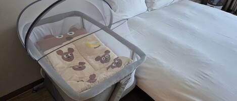 A baby crib with a canopy, a white bed with pillows, and a wooden floor.